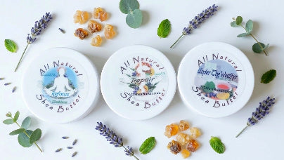 Three containers of 'All Natural' body butter with lavender, eucalyptus, and leaves and frankincense resin pieces on a white background.