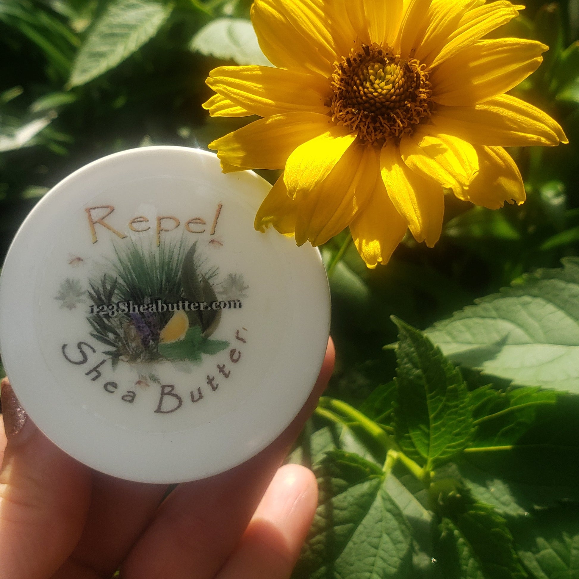 Hand holding a Repel shea butter travel size  with a yellow flower in the background