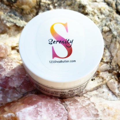 A jar of Serenity shea butter cream with a logo on the lid, placed on a background of stones.