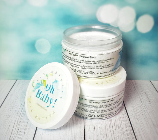 A top jar of 'Oh Baby!' fragrance-free gentle cream is open with its lid off, showing the product. The label has a blue and green design with the product name and a note that it's made with 100% organic shea butter and coconut oil.
