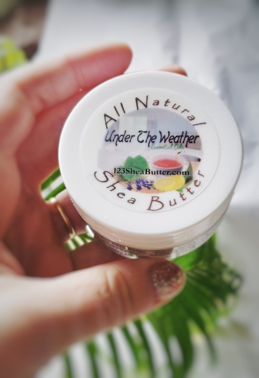 Hand holding a jar of 'All Natural Shea Butter' by 'Under The Weather'.