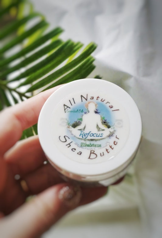 Hand holding a jar of All Natural Shea Butter Refocus 2 oz jar with a palm leaf in the background